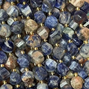 May include: Strands of faceted sodalite beads in shades of blue, grey, and brown. The beads are strung together with gold-coloured string, creating a necklace or bracelet. The gemstones have a geometric shape.