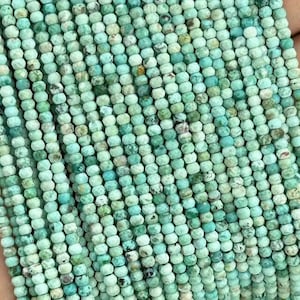 Puede incluir: Una hebra de cuentas de turquesa, cada cuenta es pequeña y redonda con un color verde y azul moteado.