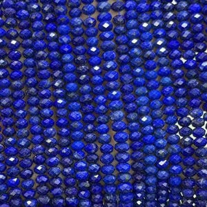 May include: A strand of deep blue lapis lazuli beads, each featuring a faceted cut that creates a reflective surface. The beads are uniform in size and shape, arranged in a long, vertical line to showcase the intense, saturated cobalt color.