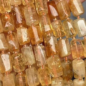 Può includere: Una collana di perle di citrino dorate, ogni perla è sfaccettata e ha una forma rettangolare. Le perle sono infilate su un filo e hanno un aspetto naturale e grezzo.
