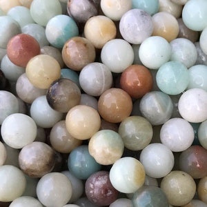 May include: A close-up of a strand of round, multi-colored beads. The beads are a mix of green, brown, white, and beige. The beads are all about the same size and are arranged in a random pattern.