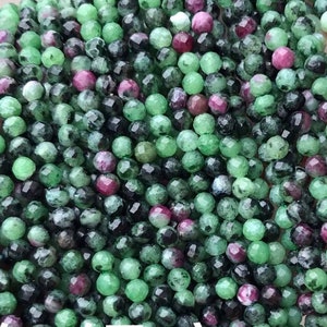 May include: Close-up of ruby zoisite beads in green, black, and red hues. The small, faceted beads create a shimmering effect. The text "Ruby zoisite" is visible in white.