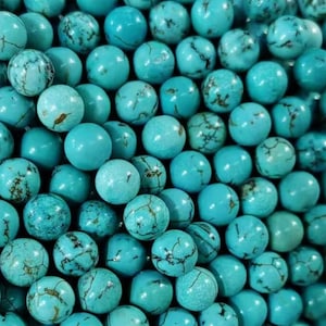 May include: A strand of turquoise beads, each bead is round and has a mottled blue-green colour. The beads are arranged in a pile, showing the texture and colour of the beads.