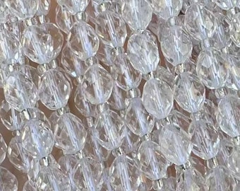 May include: Strands of clear, faceted crystal beads. The beads are strung together, creating a shimmering, decorative element. The beads are held in a hand, suggesting a craft or jewelry-making project.