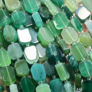 Puede incluir: Una hebra de cuentas de ágata verde, cada cuenta es un cuadrado con bordes redondeados. Las cuentas son una mezcla de tonos verdes claros y oscuros.