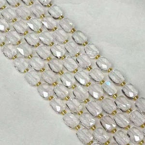 May include: Clear, faceted crystal beads strung together with gold-colored connectors. The beads are oval-shaped and arranged in parallel rows. The background is a soft, white fabric. This item is likely a decorative trim or embellishment.