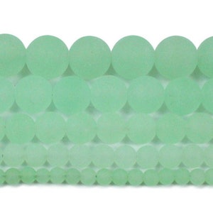 May include: A strand of round, light green glass beads. The beads are smooth and have a frosted finish.