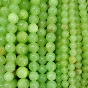 Peut inclure: Gros plan sur des brins de perles de pierres précieuses rondes, vert clair. Les perles ont une surface lisse et polie et varient légèrement de teinte, créant une subtile variation de couleur. Les perles sont enfilées ensemble, formant des lignes verticales.