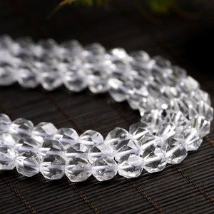 May include: A strand of clear faceted crystal beads. The beads are strung on a white thread and are arranged in a circular pattern.