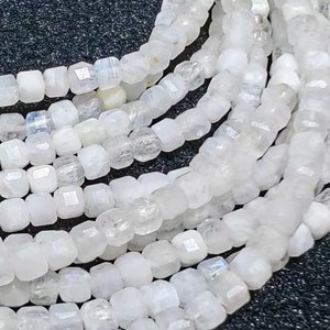 May include: A strand of white moonstone beads, each bead is faceted and has a square shape. The beads are strung together to form a long necklace.