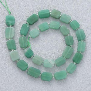 May include: A strand of green aventurine gemstone beads. The beads are rectangular with rounded edges and vary in shades of green. The beads are strung on a green cord, creating a necklace or bracelet.