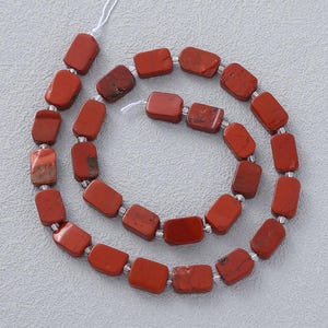 May include: A strand of rectangular, reddish-brown gemstone beads. The beads are strung together with small, clear spacers. The gemstones have a slightly mottled appearance, with variations in color and texture. The beads are arranged in a spiral.