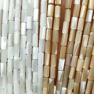 May include: Close-up of strands of rectangular beads in shades of white and tan. The beads are strung together, creating a textured surface. The beads are uniform in size and shape, and the colour variations add visual interest.