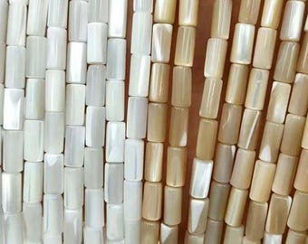 May include: Close-up of strands of rectangular beads in shades of white and tan. The beads are strung together, creating a textured surface. The beads are uniform in size and shape, and the color variations add visual interest.