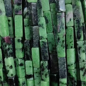 May include: Strands of green and black rectangular beads. The beads are strung together with green thread. The beads have a mix of green and black colors, with some beads having a reddish hue. The beads are likely made of a natural stone.