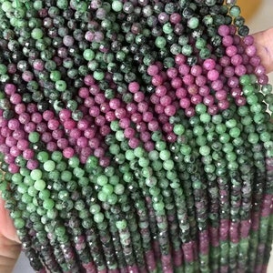 Könnte beinhalten: Eine Strähne aus grünen und rosafarbenen Edelsteinperlen. Die Perlen sind facettiert und haben eine runde Form. Die Strähne ist etwa 40 cm lang.