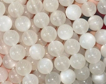May include: A strand of white moonstone beads, each bead is round and smooth. The beads are strung together on a clear thread.
