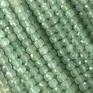 Può includere: Una collana di perline di pietra preziosa sfaccettata verde chiaro. Le perline sono di forma quadrata e hanno una finitura liscia e lucida.