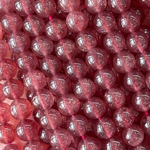 Puede incluir: Una hebra de cuentas de cuarzo fresa 5A. Las cuentas son redondas y translúcidas, de color rosa claro. Las cuentas están enhebradas en un cordón elástico transparente.