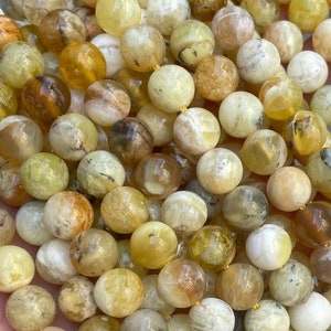 May include: A strand of round, yellow-green opal beads. The beads are approximately 6mm in diameter and have a natural, irregular shape.