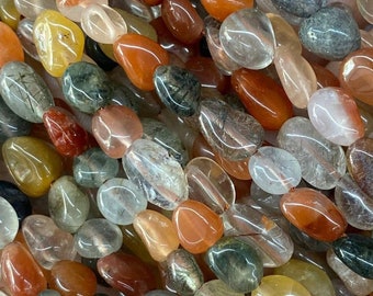 Op de afbeelding: Een streng kleurrijke fantoomkwarts kralen. De kralen zijn ovaalvormig en hebben een doorschijnende uitstraling. De kleuren van de kralen omvatten groen, rood, oranje en geel. De kralen zijn in een willekeurig patroon gerangschikt. De tekst "Colorful Phantom Quartz" staat onder de kralen.