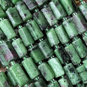 Puede incluir: Una hebra de cuentas de piedras preciosas verdes y negras, cada cuenta tiene forma de prisma rectangular. Las cuentas están enhebradas en un cordón elástico transparente.