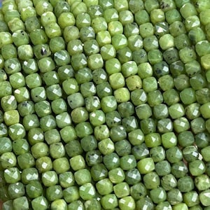 Puede incluir: Una hebra de cuentas de jade verde, cada cuenta está facetada y tiene forma cuadrada. Las cuentas están enhebradas en un hilo transparente y tienen aproximadamente 4 mm de tamaño.