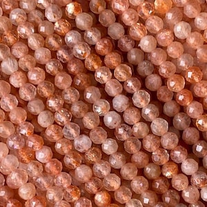 May include: A strand of orange sunstone beads, each bead is faceted and has a shimmery, iridescent finish. The beads are strung on a clear thread and are ready for jewelry making.