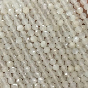 Peut inclure: Un brin de perles de pierre de lune blanche, chaque perle est facetée et présente un léger éclat iridescent.