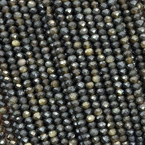 Peut inclure: Un brin de perles de pierres précieuses facettées noires avec un éclat doré. Les perles sont petites et de taille uniforme, créant un look élégant et raffiné.