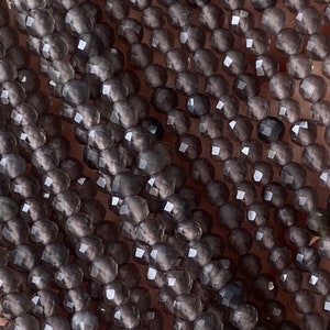 May include: A strand of gray faceted gemstone beads. The beads are small and round, and they have a smooth, polished finish.