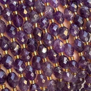 May include: Strands of faceted amethyst beads with gold-colored spacers. The beads are a deep purple color and have a geometric cut, reflecting light. The beads are strung together, creating a necklace or bracelet.