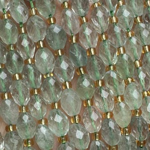 Può includere: Primo piano di più fili di perline ovali sfaccettate nei toni del verde pallido e trasparente. Le perline sono separate da piccoli distanziatori color oro. Le perline sono infilate insieme, creando un aspetto delicato ed elegante. Le perline sono probabilmente realizzate in pietra preziosa o cristallo.