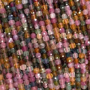 May include: A multi-strand collection of small, faceted, square-shaped tourmaline beads in a vibrant spectrum of pink, green, yellow, and brown hues. Each bead features a polished, reflective surface that catches the light, creating a shimmering effect across the entire length of the strands.