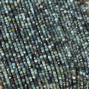 Può includere: Fili di piccole perline quadrate nei toni del verde acqua, blu e grigio. Le perline sono infilate insieme, creando una superficie strutturata. Le perline sono tenute in una mano, mostrando il loro colore e la loro forma.