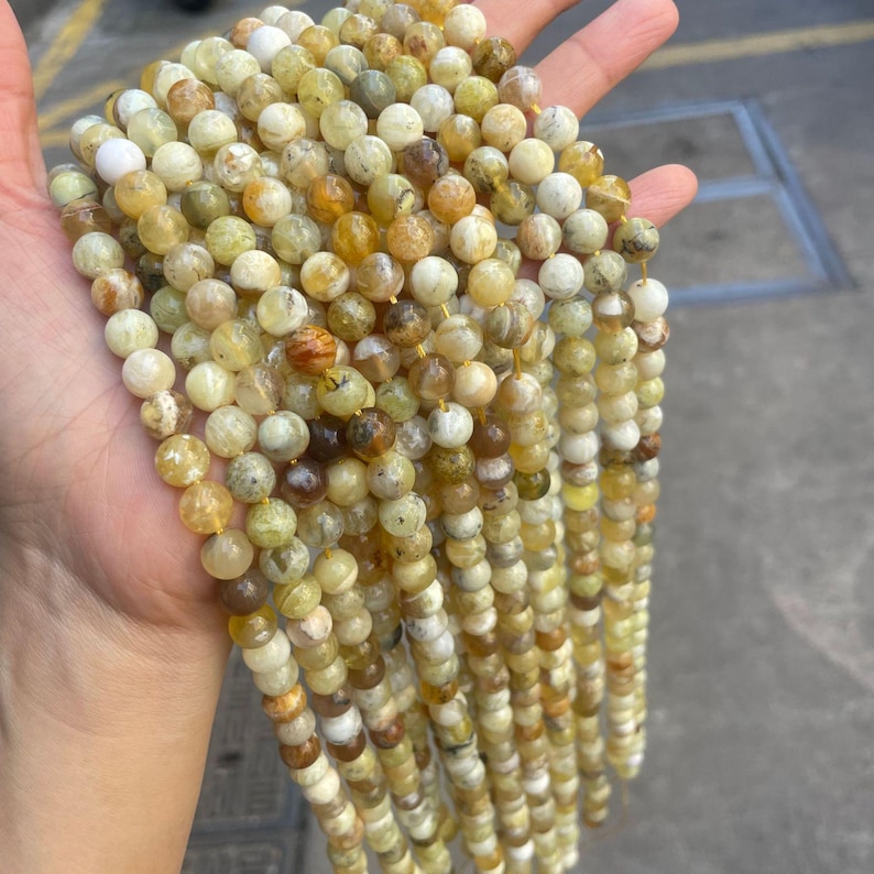 May include: A strand of round, yellow and white opal beads. The beads are approximately 6mm in diameter and have a natural, irregular shape.