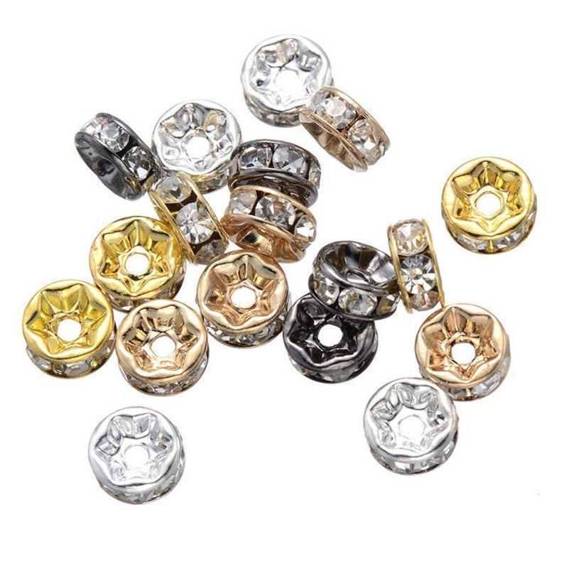 Pu&ograve; includere: Assortimento di cappucci per perline in metallo con accenti di strass trasparenti. I cappucci per perline sono di vari colori, tra cui oro, argento e nero.