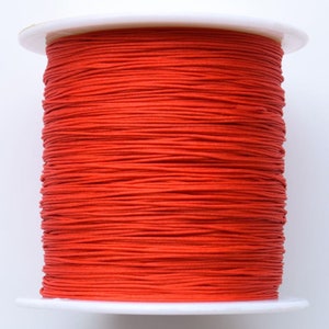 Puede incluir: Una bobina de cord&oacute;n el&aacute;stico rojo brillante, enrollada apretadamente en una bobina de pl&aacute;stico blanco.