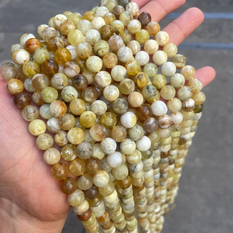 May include: A strand of round, yellow-green opal beads. The beads are approximately 6mm in diameter and have a natural, irregular shape.