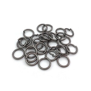 Peut inclure: Un ensemble de petits anneaux de saut gris fonc&eacute;, dispos&eacute;s sur une surface blanche. Les anneaux sont circulaires avec une petite ouverture, sugg&eacute;rant une utilisation pour la fabrication de bijoux ou l'artisanat. Le m&eacute;tal a une finition mate.