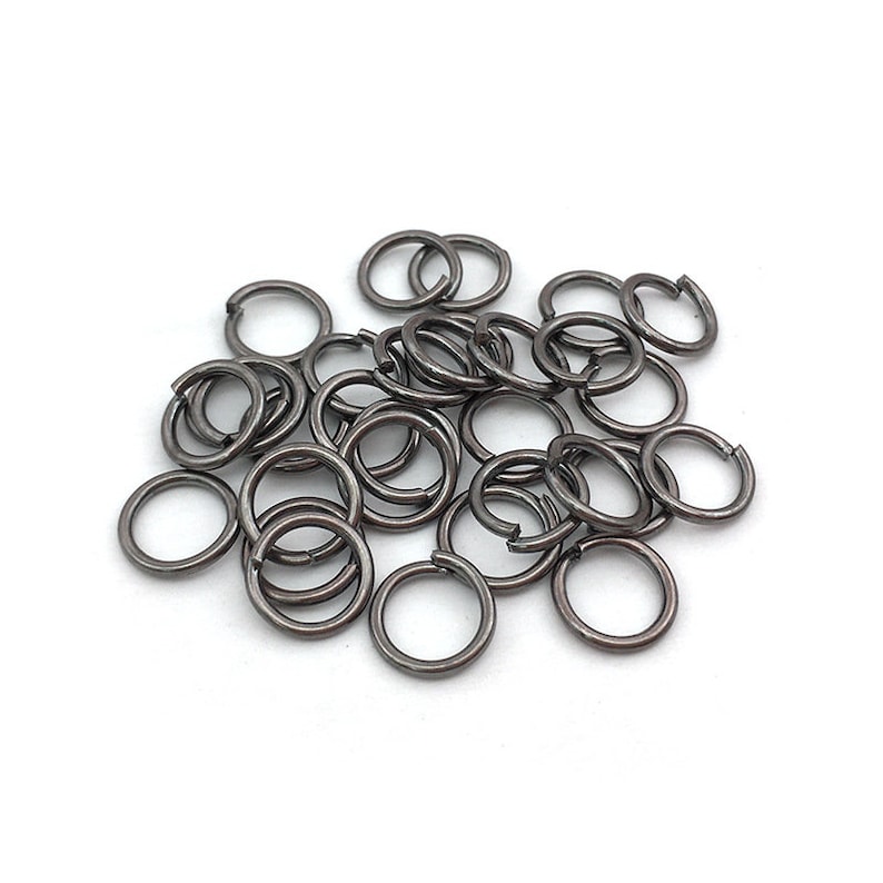 Peut inclure: Un ensemble de petits anneaux de saut gris fonc&eacute;, dispos&eacute;s sur une surface blanche. Les anneaux sont circulaires avec une petite ouverture, sugg&eacute;rant une utilisation pour la fabrication de bijoux ou l'artisanat. Le m&eacute;tal a une finition mate.