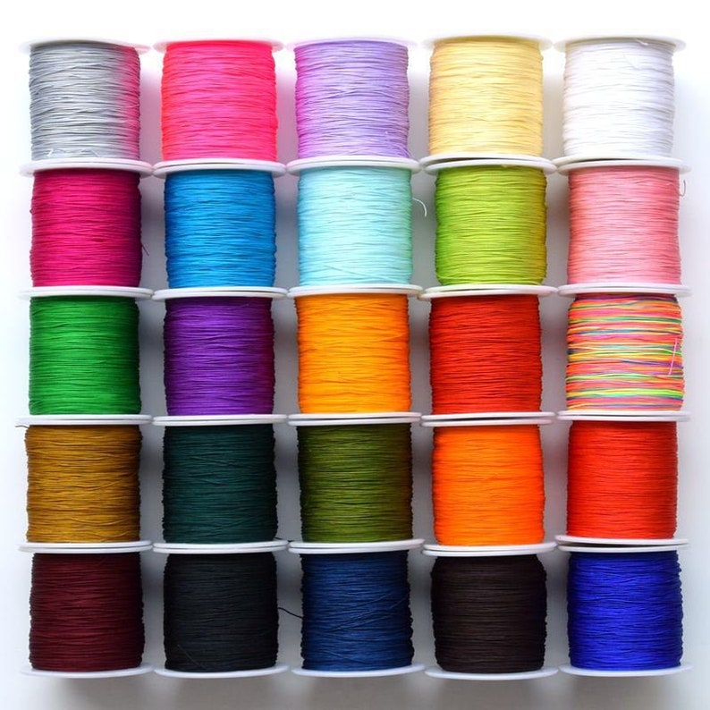 Puede incluir: Una colecci&oacute;n de 25 carretes de hilo de colores, cada uno enrollado alrededor de una bobina de pl&aacute;stico blanca. Los carretes est&aacute;n dispuestos en una cuadr&iacute;cula, con cinco filas de cinco carretes cada una. Los colores del hilo incluyen rojo, naranja, amarillo, verde, azul, morado, rosa, blanco, negro y marr&oacute;n.