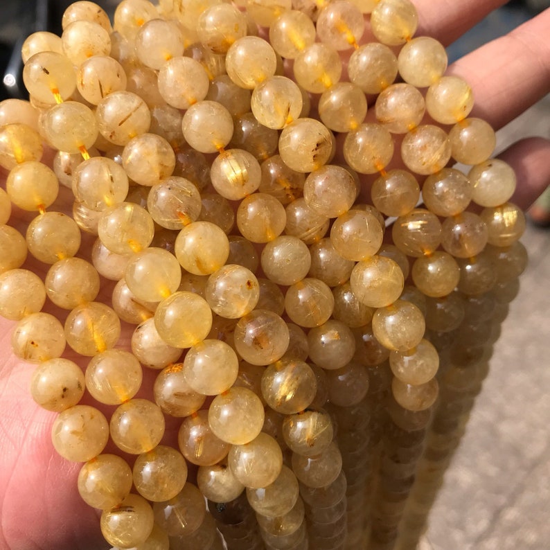 May include: A strand of golden rutilated quartz beads. The beads are round and translucent, with golden inclusions that shimmer in the light.