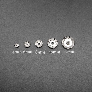 Pu&ograve; includere: Cinque decorazioni metalliche argentate di diverse dimensioni, che vanno da 4 mm a 12 mm. Le decorazioni sono rotonde con un centro rialzato e un bordo decorativo.
