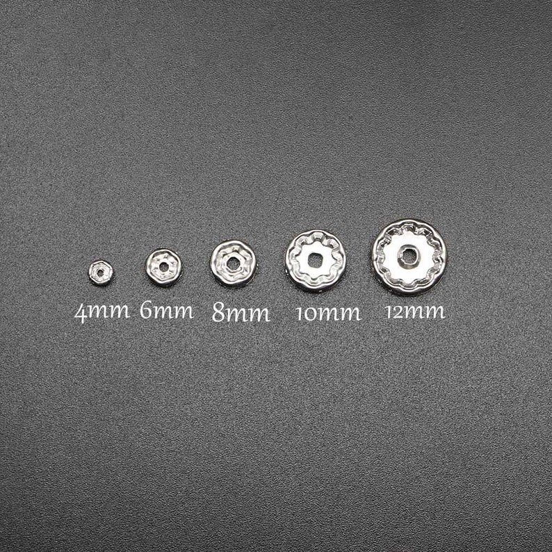 Pu&ograve; includere: Cinque decorazioni metalliche argentate di diverse dimensioni, che vanno da 4 mm a 12 mm. Le decorazioni sono rotonde con un centro rialzato e un bordo decorativo.