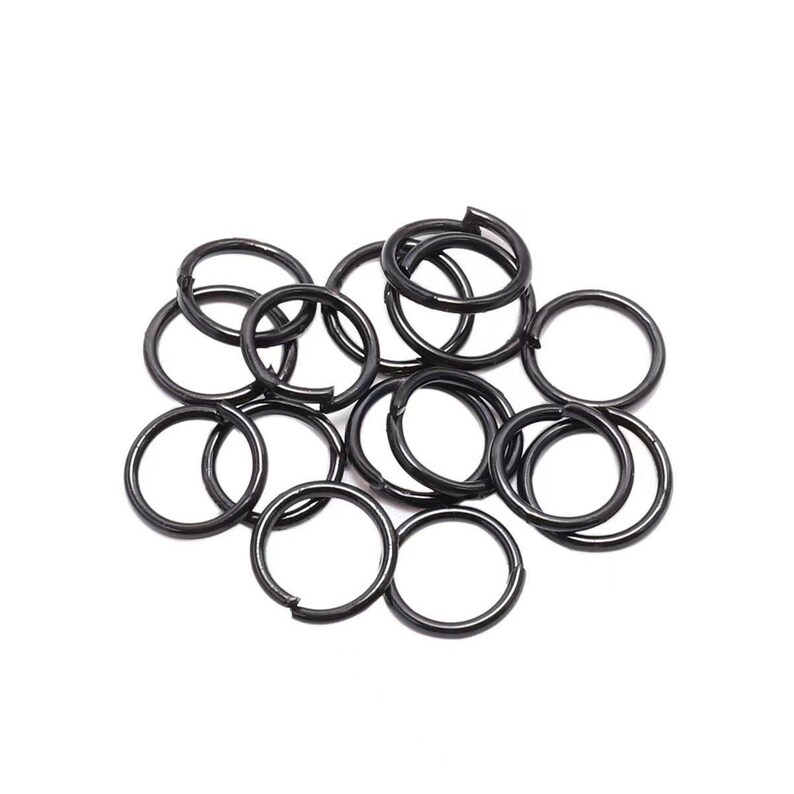 Peut inclure: Un ensemble de petits anneaux fendus en m&eacute;tal noir, dispers&eacute;s sur un fond blanc. Ces anneaux circulaires sont fendus, ce qui permet de les ouvrir et de les fermer. Ils sont probablement utilis&eacute;s pour des porte-cl&eacute;s ou la fabrication de bijoux.