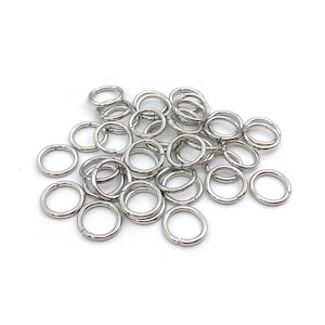 Peut inclure: Un ensemble de petits anneaux de saut argent&eacute;s, dispos&eacute;s sur une surface blanche. Les anneaux sont circulaires et fendus pour pouvoir &ecirc;tre ouverts et ferm&eacute;s. Ils sont probablement utilis&eacute;s pour la fabrication de bijoux ou d'autres travaux manuels.