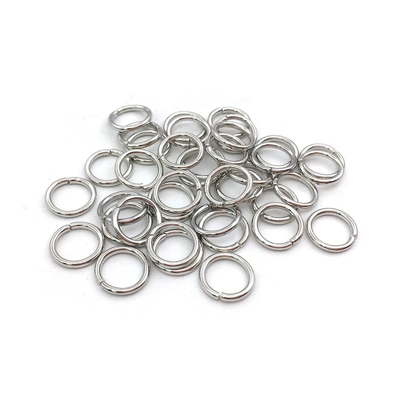 Peut inclure: Un ensemble de petits anneaux de saut argent&eacute;s, dispos&eacute;s sur une surface blanche. Les anneaux sont circulaires et fendus pour pouvoir &ecirc;tre ouverts et ferm&eacute;s. Ils sont probablement utilis&eacute;s pour la fabrication de bijoux ou d'autres travaux manuels.