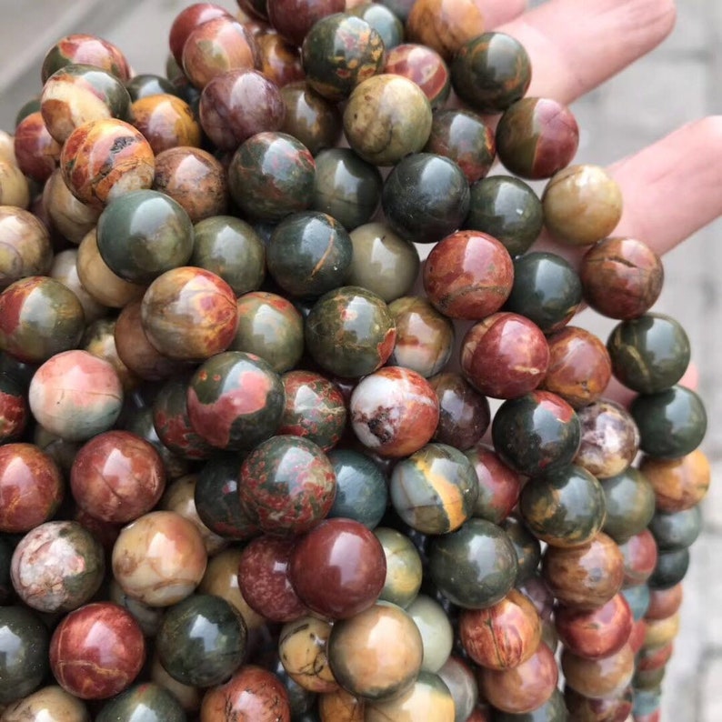 May include: A close-up of a pile of round, multi-colored, polished stones. The stones are a mix of red, green, brown, and white.