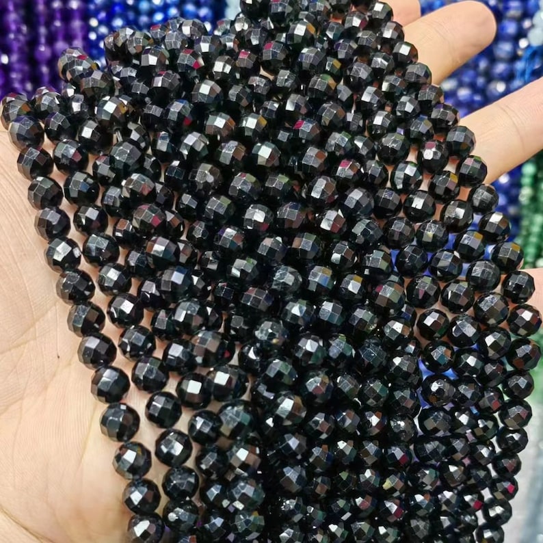 Peut inclure: Un brin de perles de pierres pr&eacute;cieuses facett&eacute;es noires. Les perles sont rondes et ont une finition brillante et iris&eacute;e.